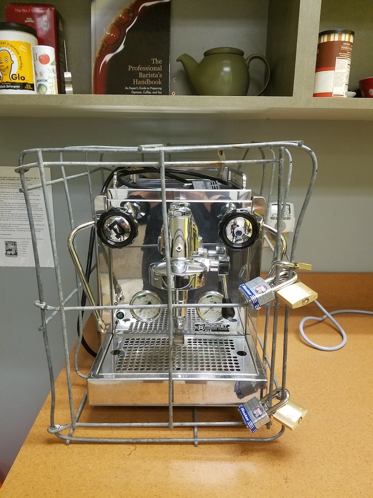 Espresso machine in a metal cage with five padlocks.